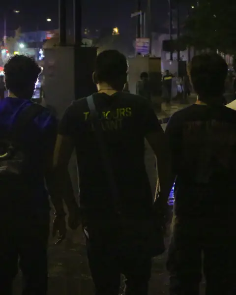 Four friends walking out together at night toward the lights.