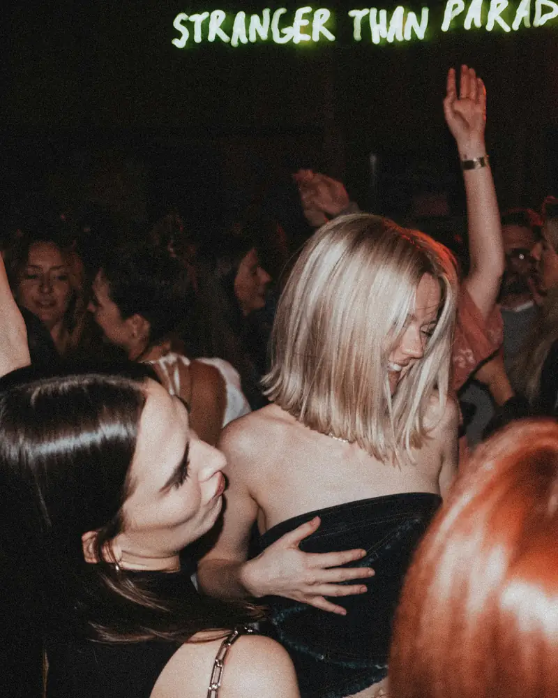 A packed small room, people dancing under a neon sign.